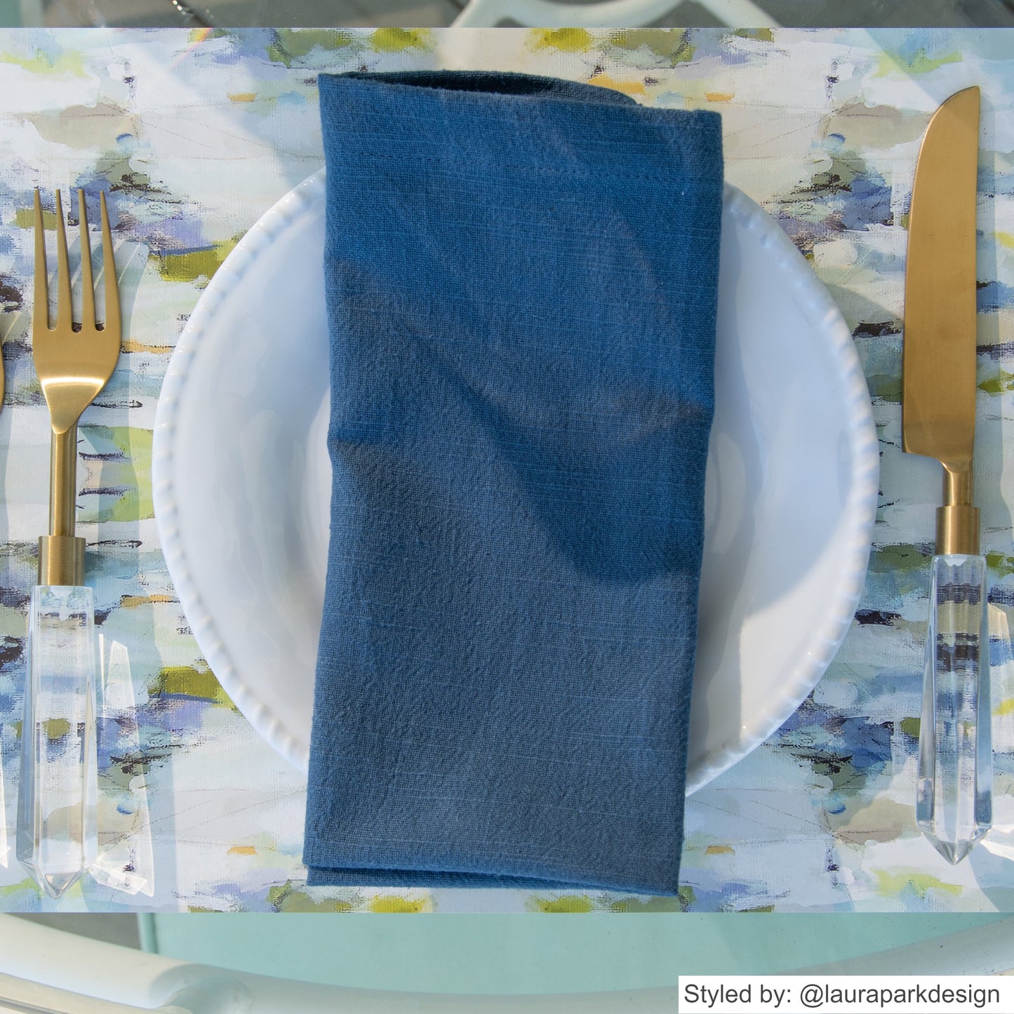 Blue and gray watercolor paper placemat layered with a white plate and dark blue napkin