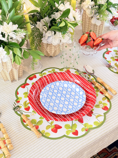 Decorative table setting with a red and white plate, green leaves, and strawberries.