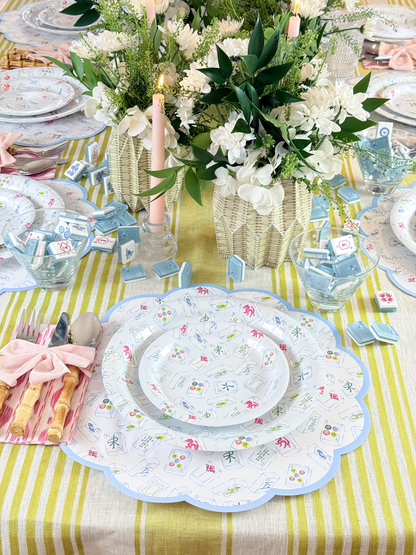 Decorative table setting with blue mahjong patterned placemats and plates, candles, and flowers on a striped tablecloth.