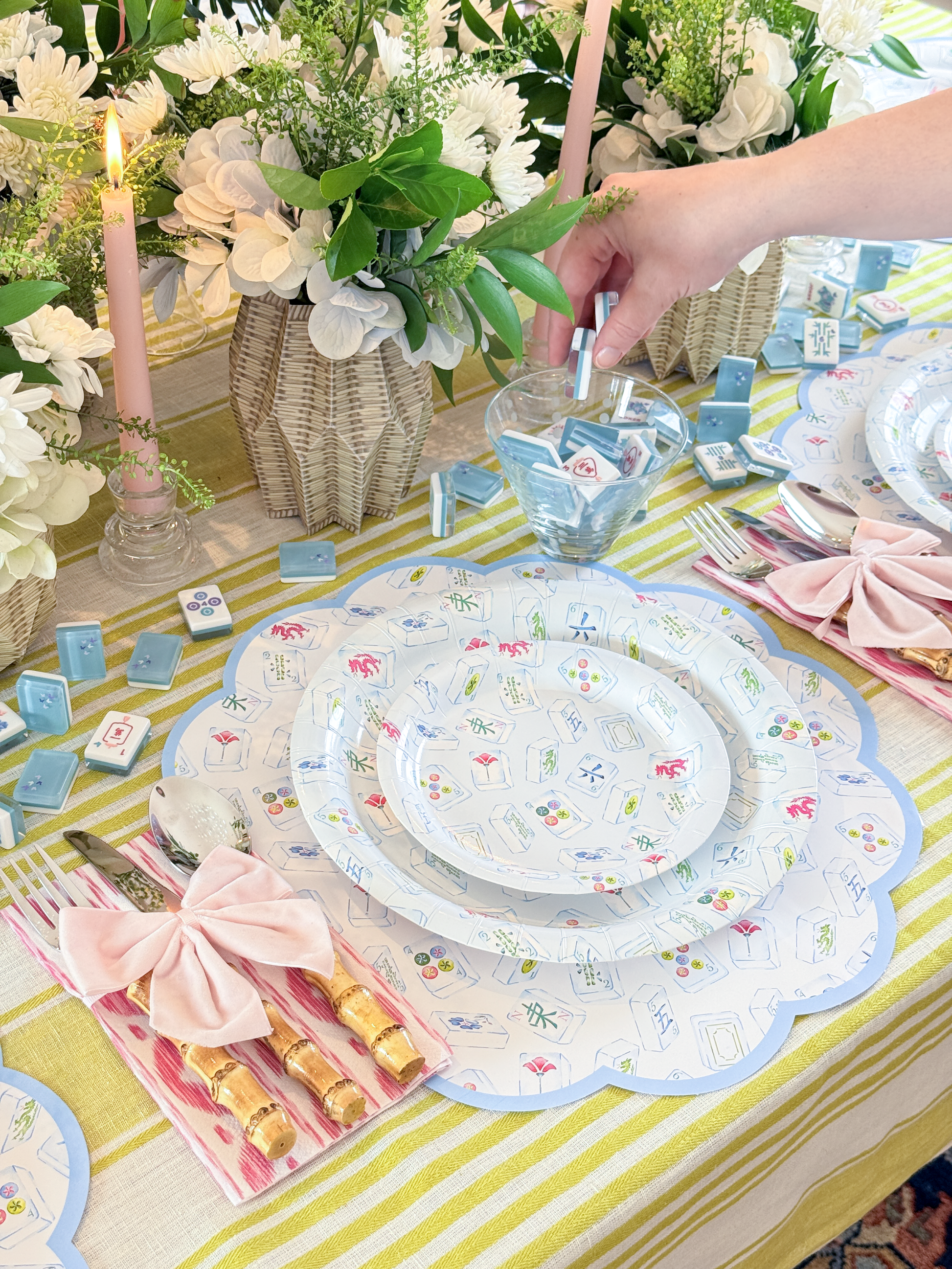 Decorative table setting with blue mahjong patterned placemats and plates, candles, and flowers on a striped tablecloth.