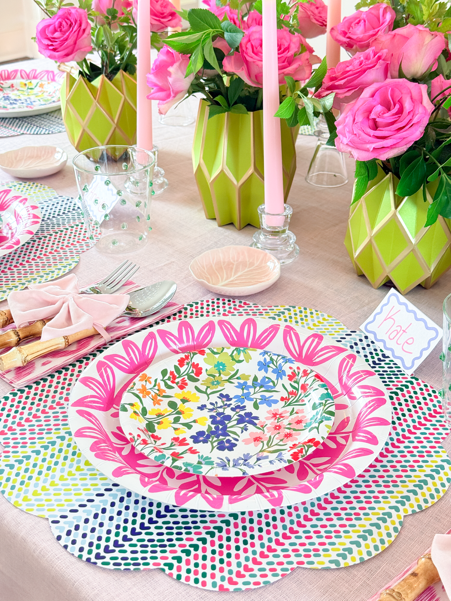 Decorative table setting with floral plates, pink candles, and colorful placemats.
