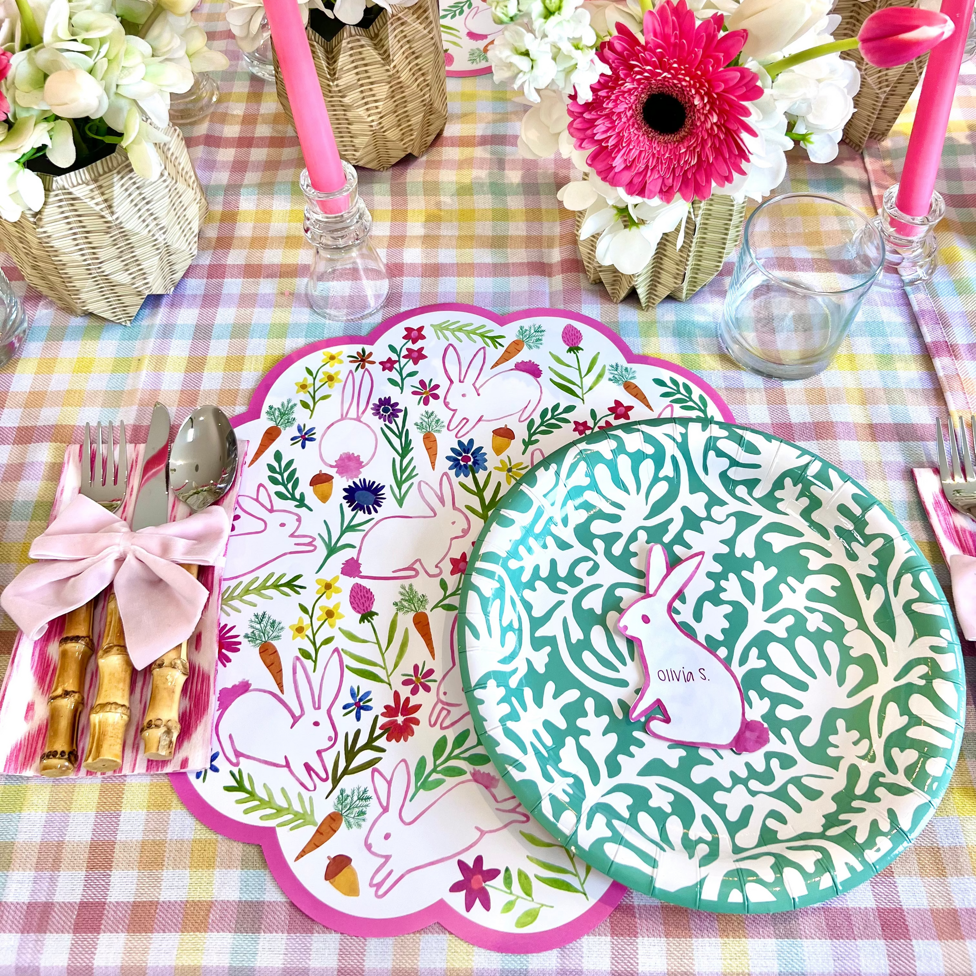 Easter-themed table setting with floral centerpieces, bunny paper placemats, teal green plates on a checkered tablecloth.