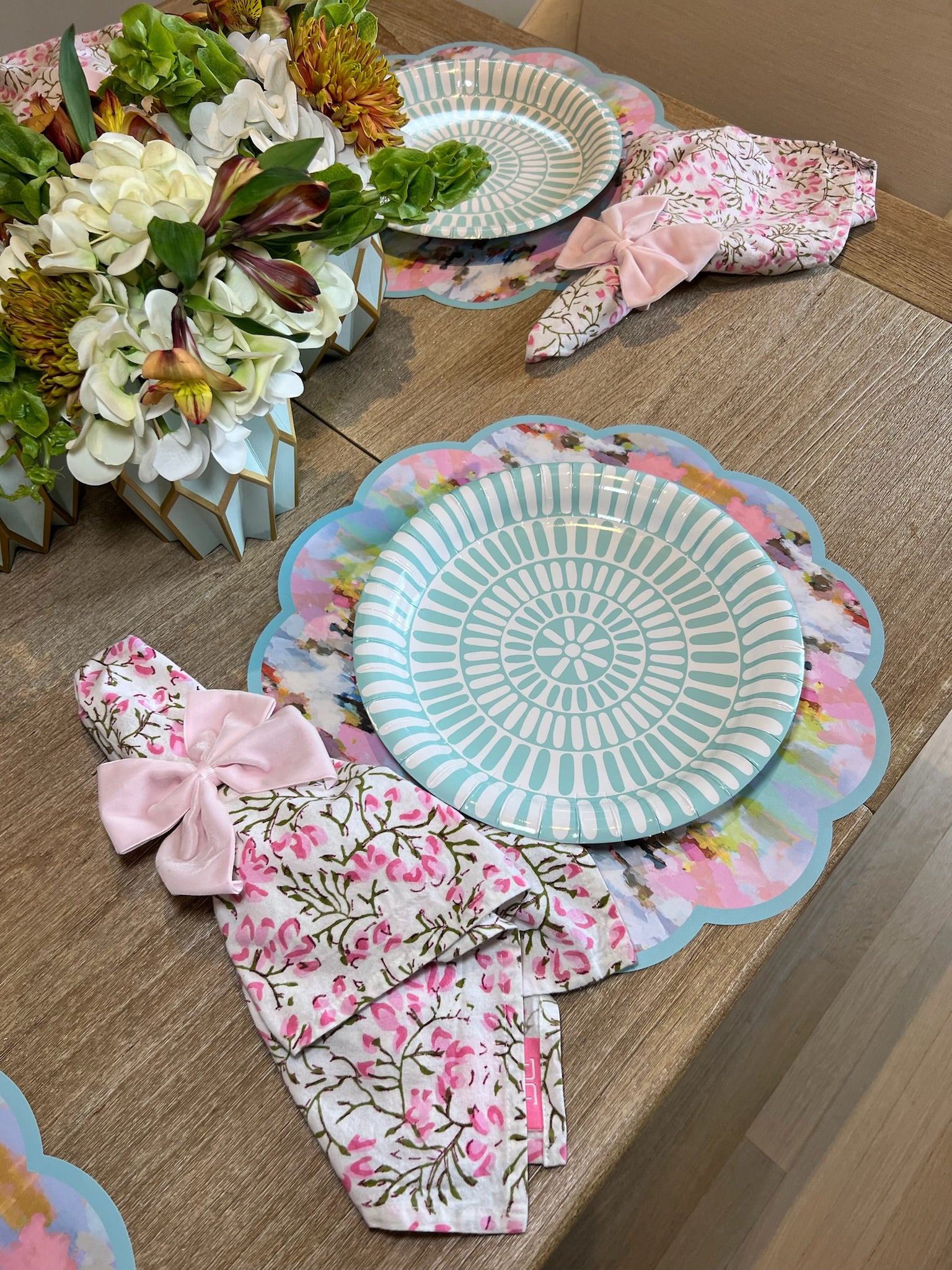 A pink and blue tablescape featuring our blue and pink watercolor paper placemat, light blue heavy duty paper plate, light pink bow napkin rings, and flower arrangement with our tiffany blue paper vase wraps