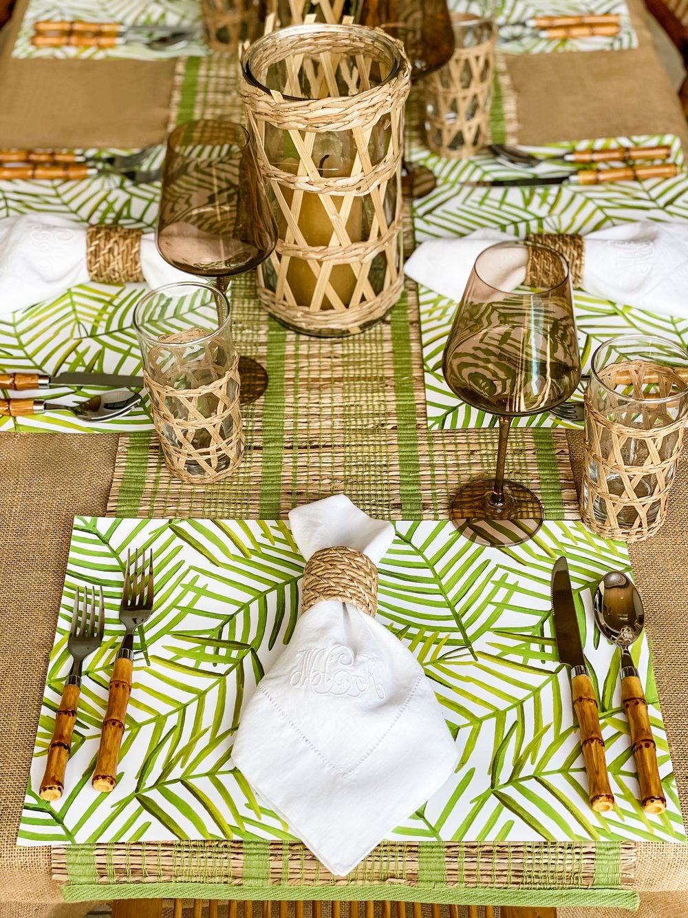 Green leaf paper placemats on a brown tablecloth with white napkins and other bamboo elements