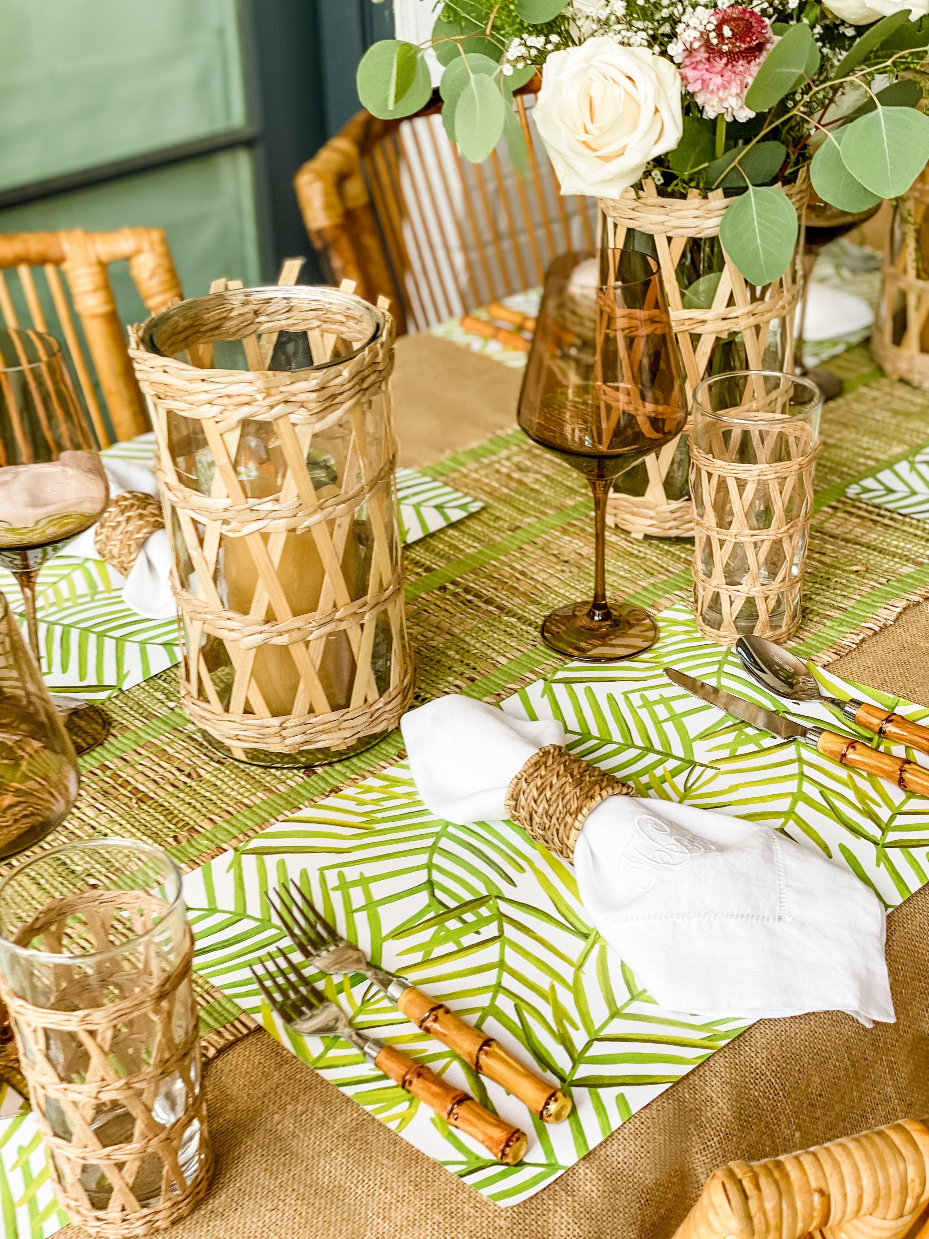 Green leaf paper placemats on a brown tablecloth with white napkins and other bamboo elements