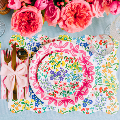 Multicolor wildflower paper plates and matching scalloped placemat styled in a table setting with gold flatware and a pink bow napkin