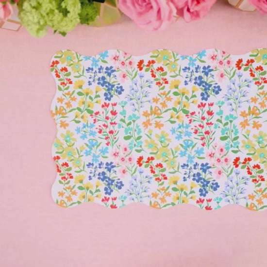 Video showing a multicolor wildflower scalloped placemat being layered with a light blue cane-weave dinner plate and a multicolor wildflower dessert plate
