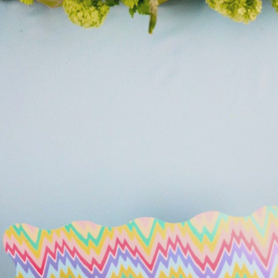 Video showing a multicolor pastel zigzag scalloped placemat being layered with a light blue cane-weave dinner plate
