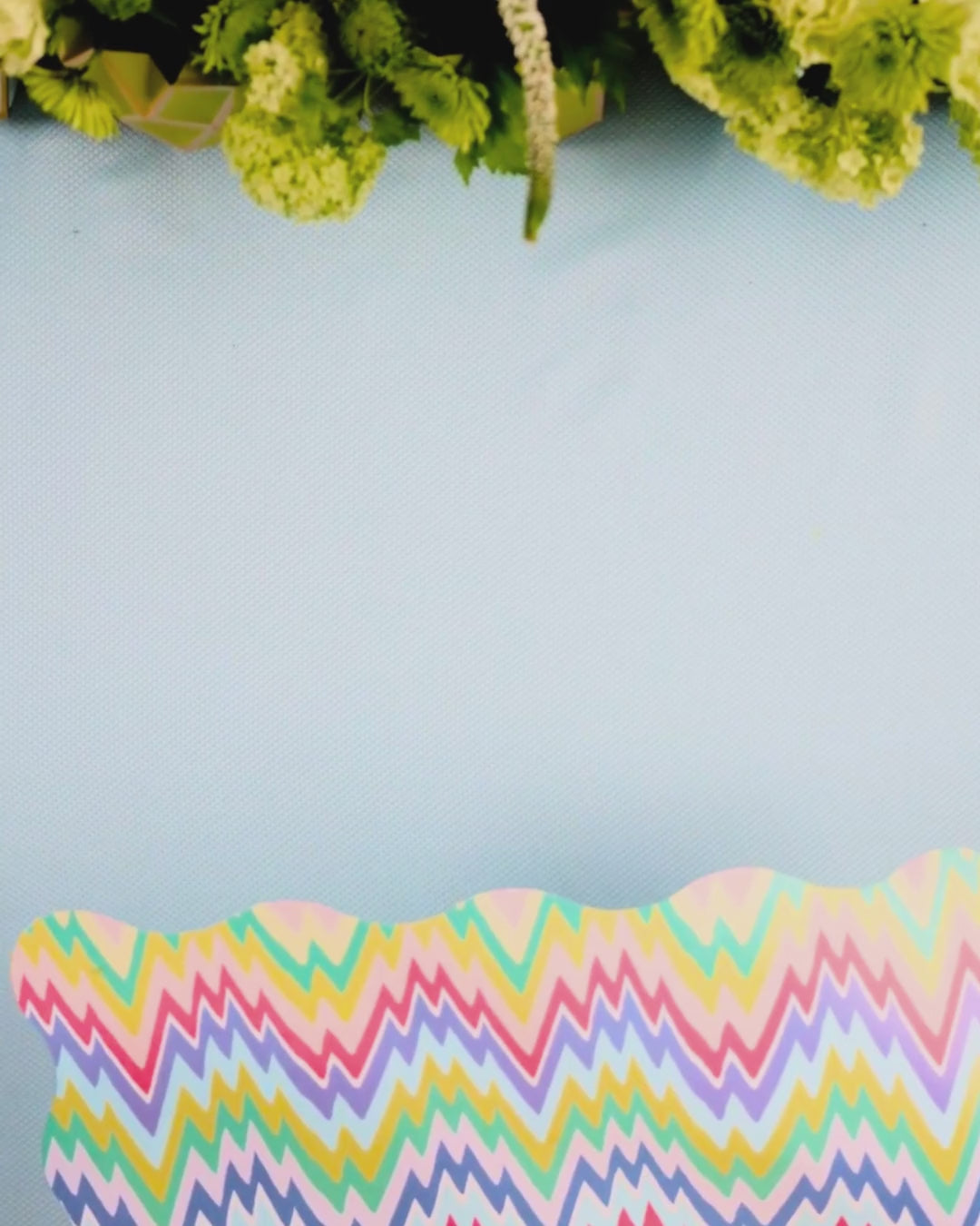 Video showing a multicolor pastel zigzag scalloped placemat being layered with a light blue cane-weave dinner plate