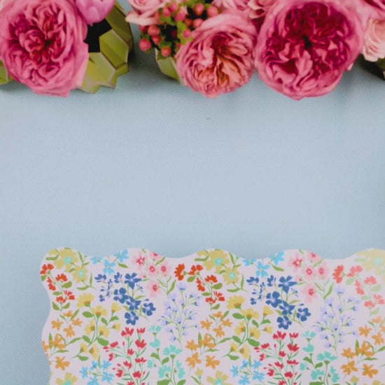 Video showing a multicolor wildflower scalloped placemat being layered with a pink botanical leaf-print dessert plate