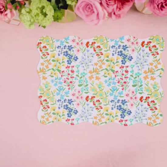Video showing a multicolor wildflower scalloped placemat being layered with a light blue cane-weave dinner plate and a multicolor wildflower dessert plate