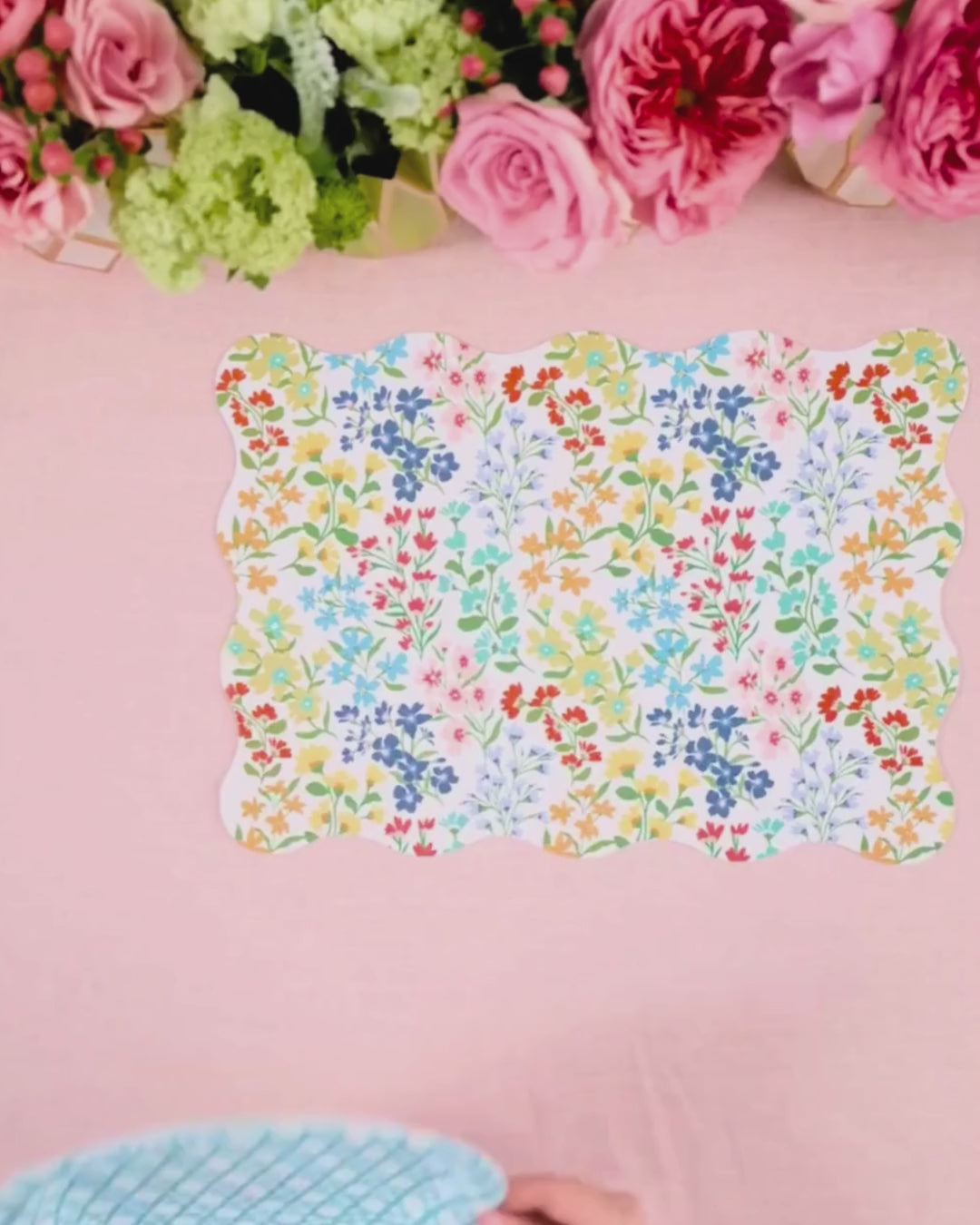 Video showing a multicolor wildflower scalloped placemat being layered with a light blue cane-weave dinner plate and a multicolor wildflower dessert plate