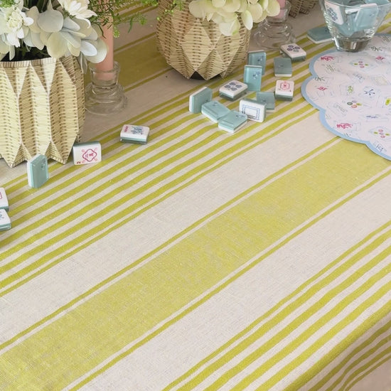 Decorative table setting with blue mahjong patterned placemats and plates, candles, and flowers on a striped tablecloth.
