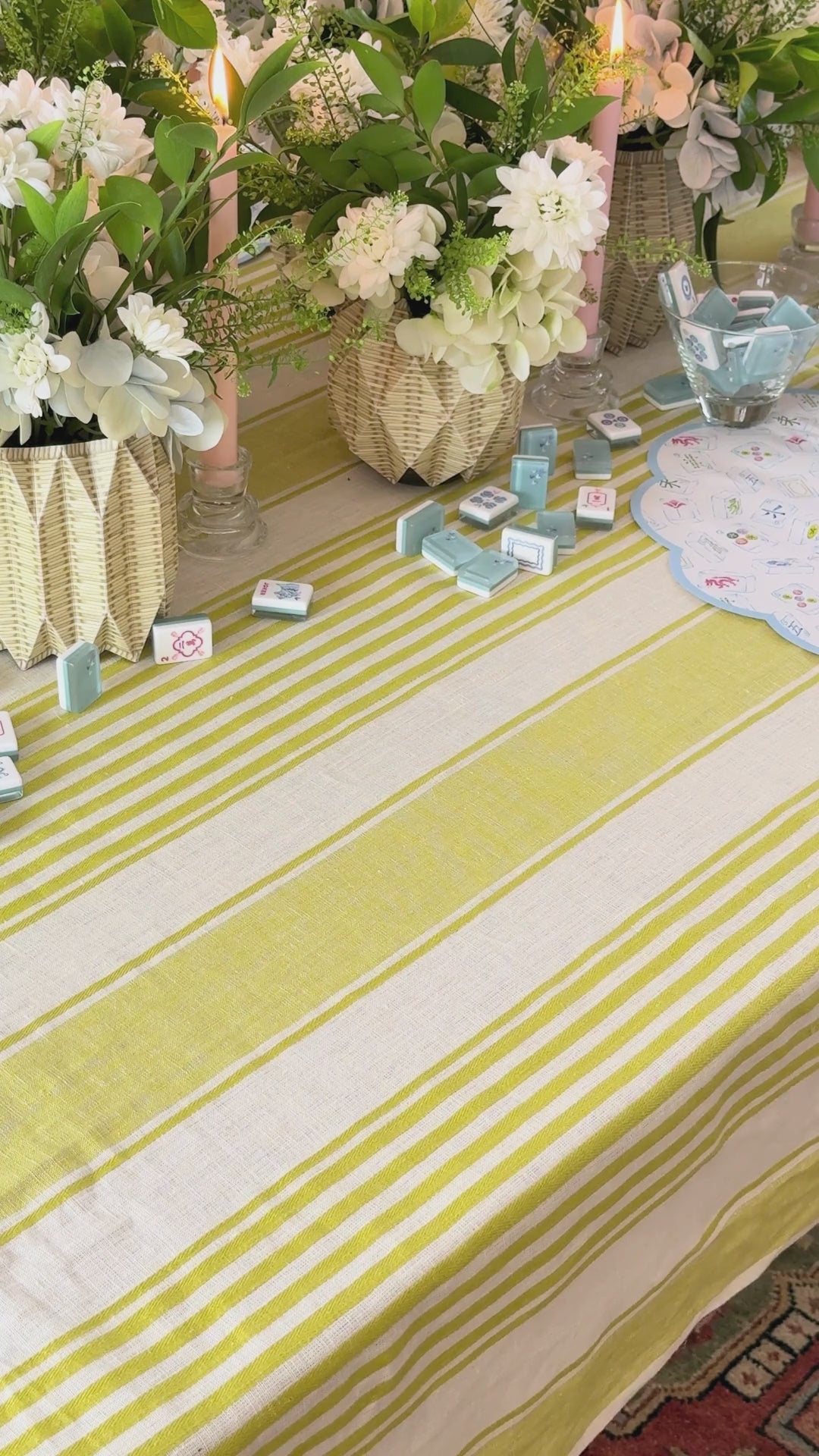 Decorative table setting with blue mahjong patterned placemats and plates, candles, and flowers on a striped tablecloth.