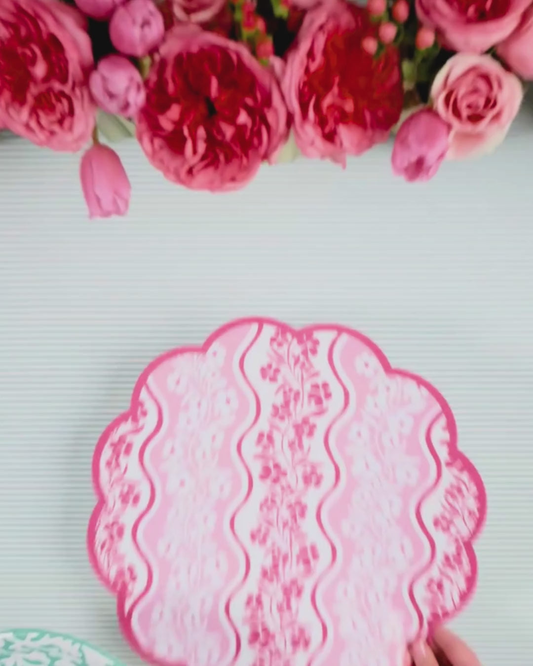 Video showing a pink wavy-stripe floral scalloped placemat being layered with a mint green abstract floral dinner plate