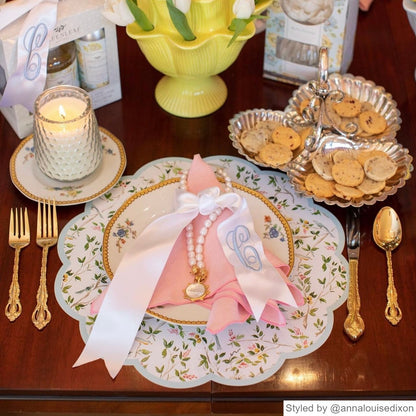 Place setting with a chinoiserie round scalloped paper placemat and pink napkin on a wood table