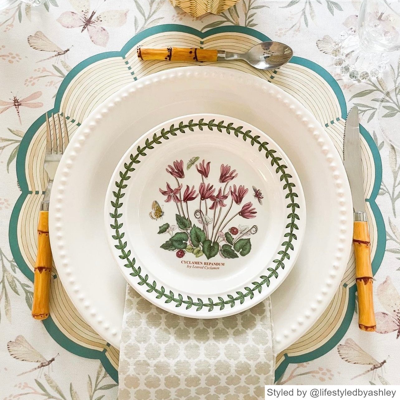 Place setting with a scalloped round wicker patterned paper placemat layered with white and pink dishes featuring flowers