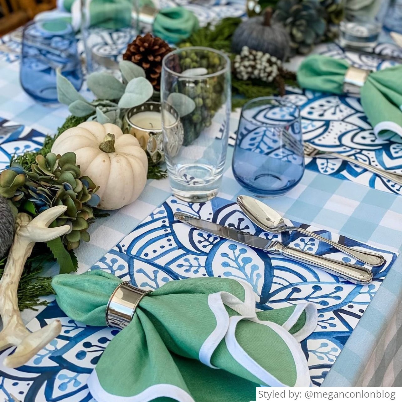 Table setting with blue and white paper placemats layered with a green napkin and other green and white fall table decor