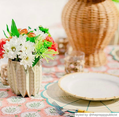 Table setting with a wicker patterned scalloped round paper placemat layered with a bamboo plate and a wicker patterned paper vase sleeve