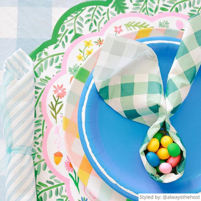 Close up of a place setting with a green gingham round scalloped placemat layered with bunny round scalloped chargers, a pastel gingham plate and a blue plate with a green gingham napkin folded into a bunny shape with colorful jelly beans