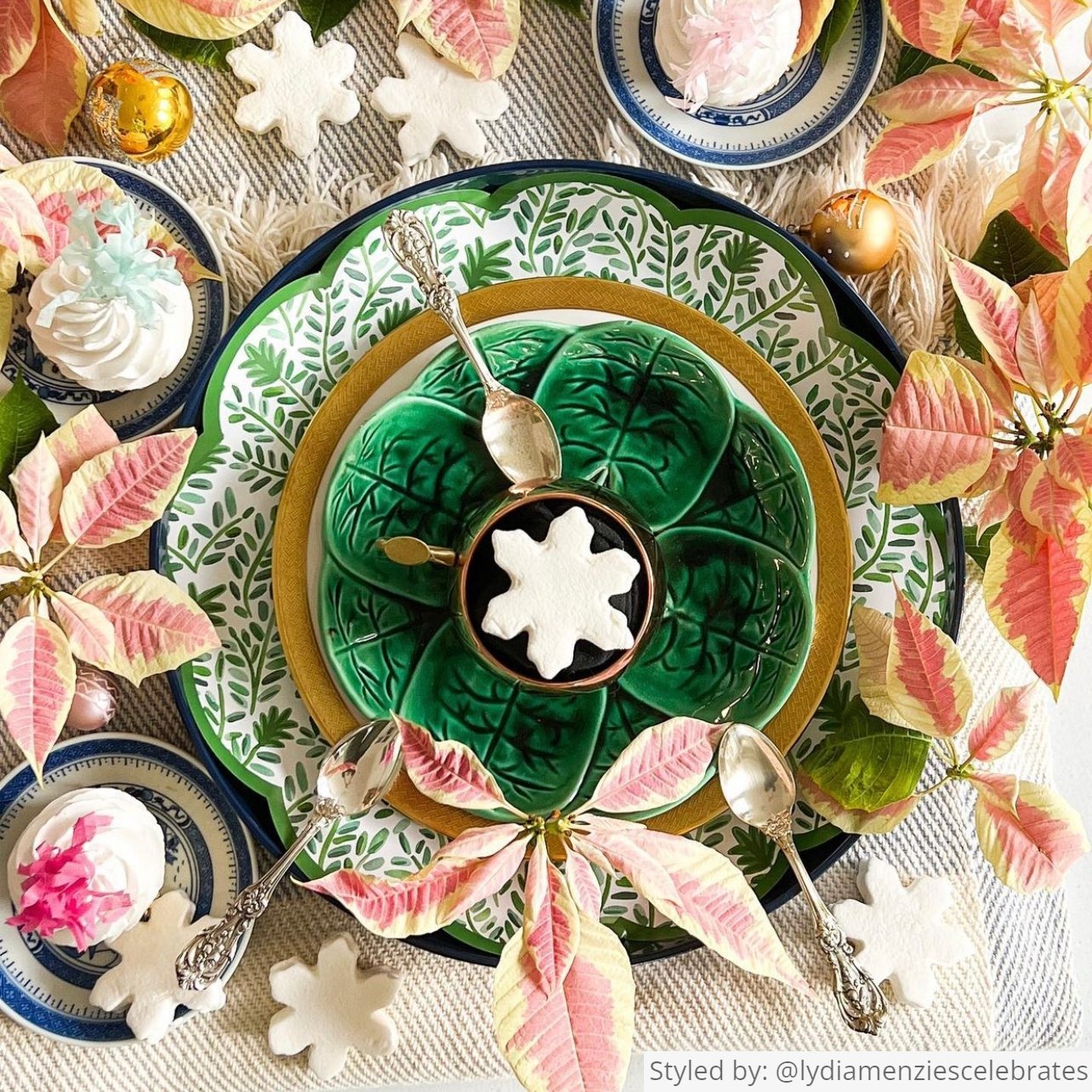 Place setting with a green vine scalloped round paper placemat layered with bowls, decorative snowflakes and poinsettias