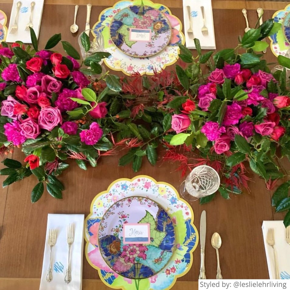 Table setting with round scalloped tobacco leaf paper placemats on a wood table with pink flowers