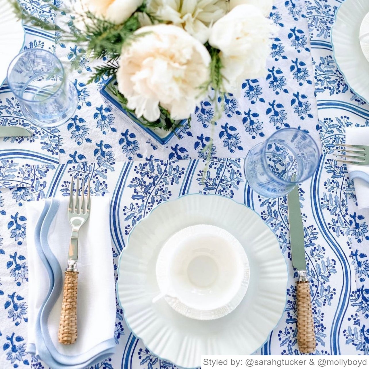 Blue and white holly paper placemat layered with white dishes and a teacup on a blue and white floral tablecloth