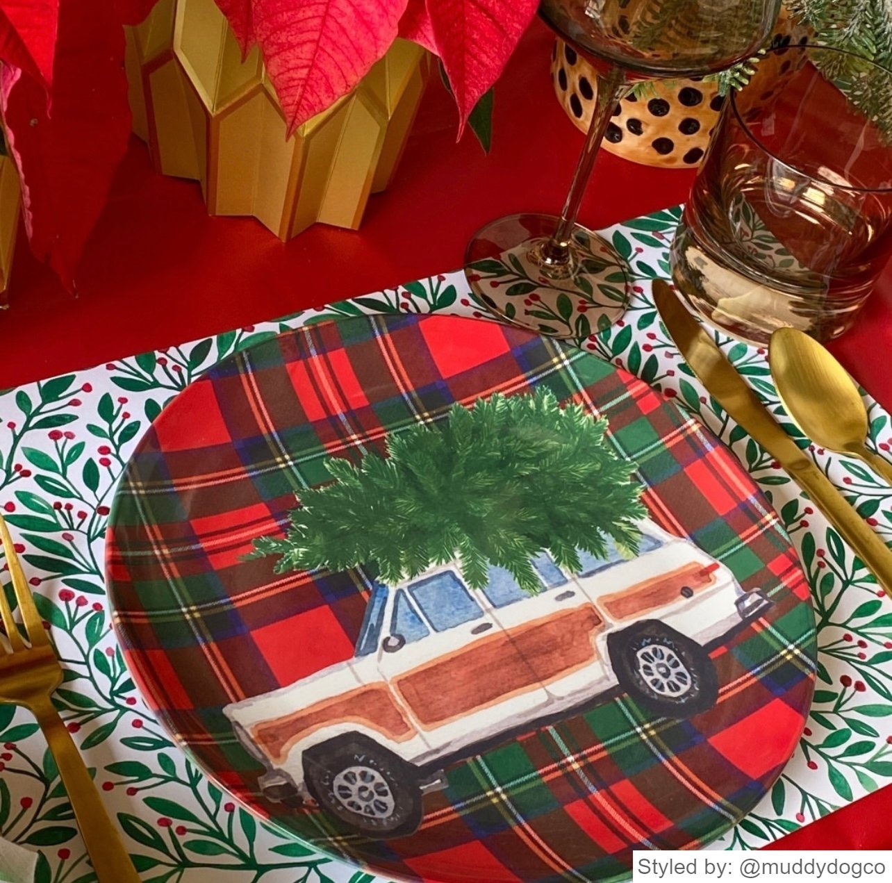 Red and green paper placemat layered with a red and black plaid plate featuring a car carrying a Christmas tree