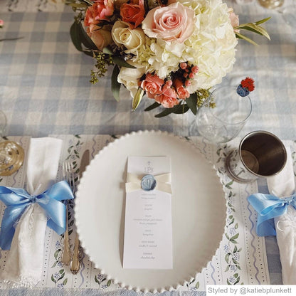 Place setting with white floral paper placemats layered with a white plate and a pink flower arrangement centerpiece