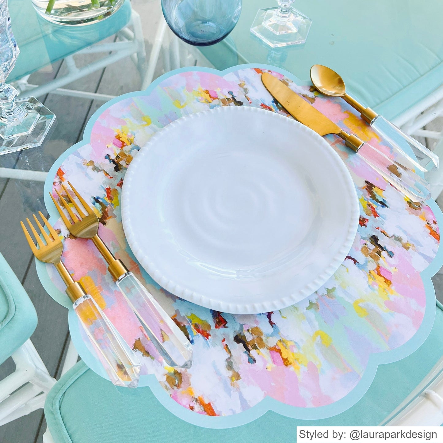 Pink and blue watercolor scalloped round paper placemat layered with a white plate and gold flatware