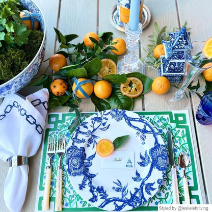 Place setting with a green and white paper placemat layered with a blue and white dish on an outdoor table with oranges