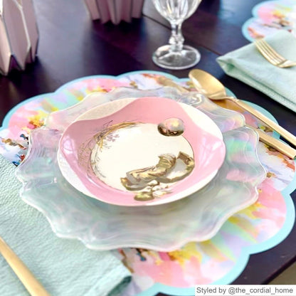 Pink and blue watercolor scalloped round paper placemat layered with pink and blue plates on a dark wood table