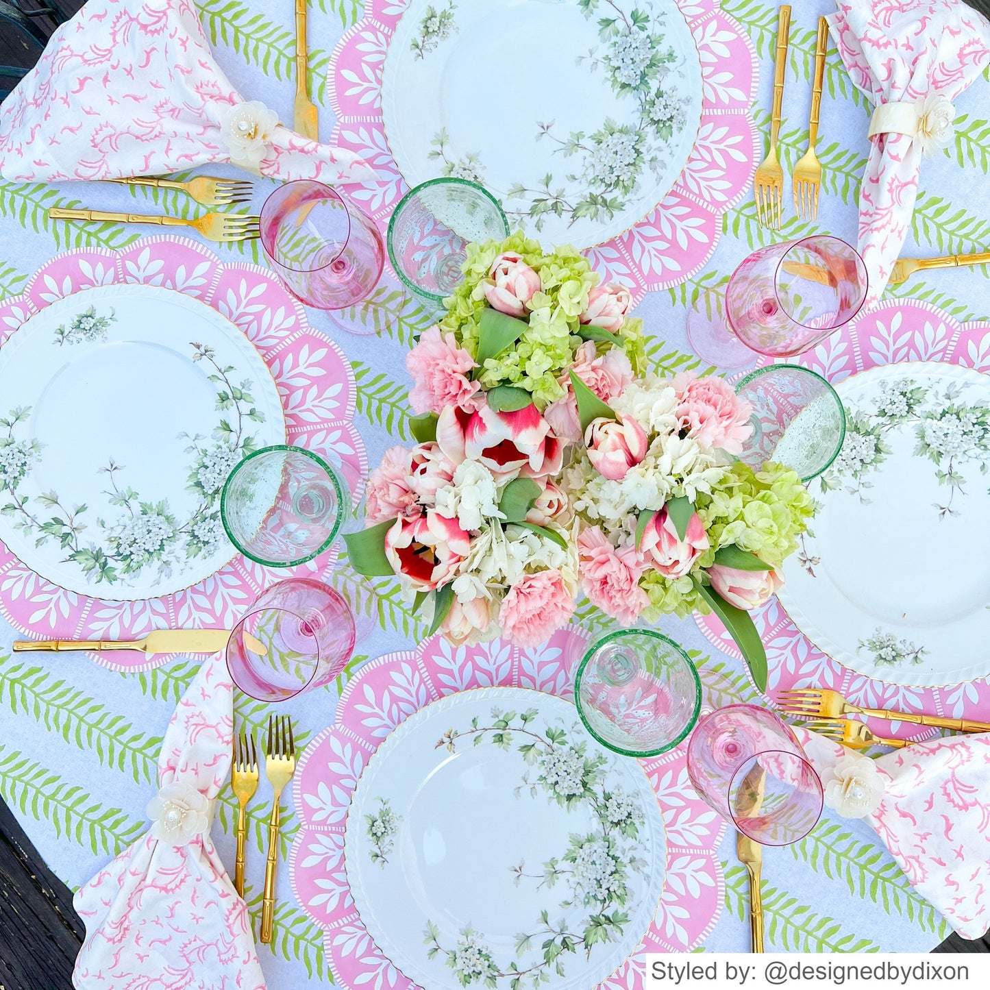 Pink and white scalloped round paper placemats on a green and white patterned tablecloth with flowers