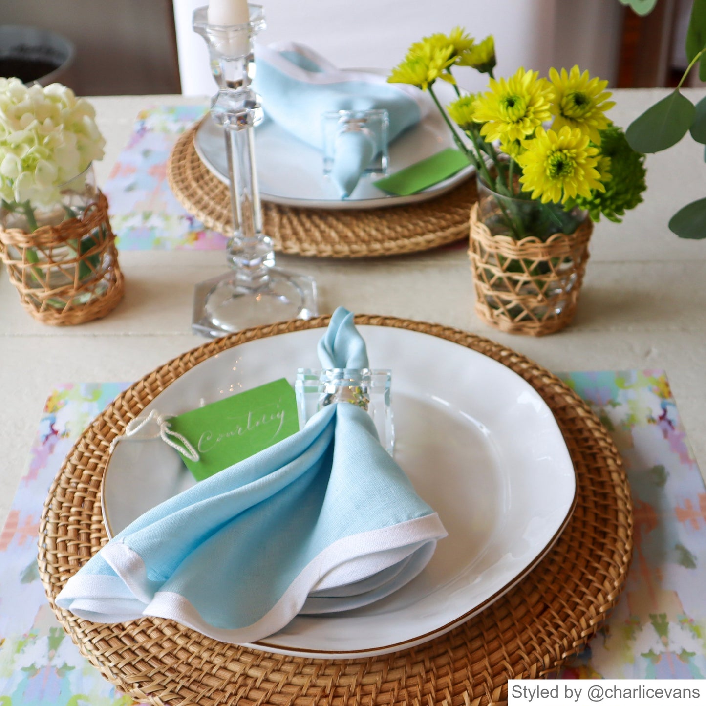 Pink and blue watercolor patterned paper placemat layered with a rattan charger, white dish and blue napkin