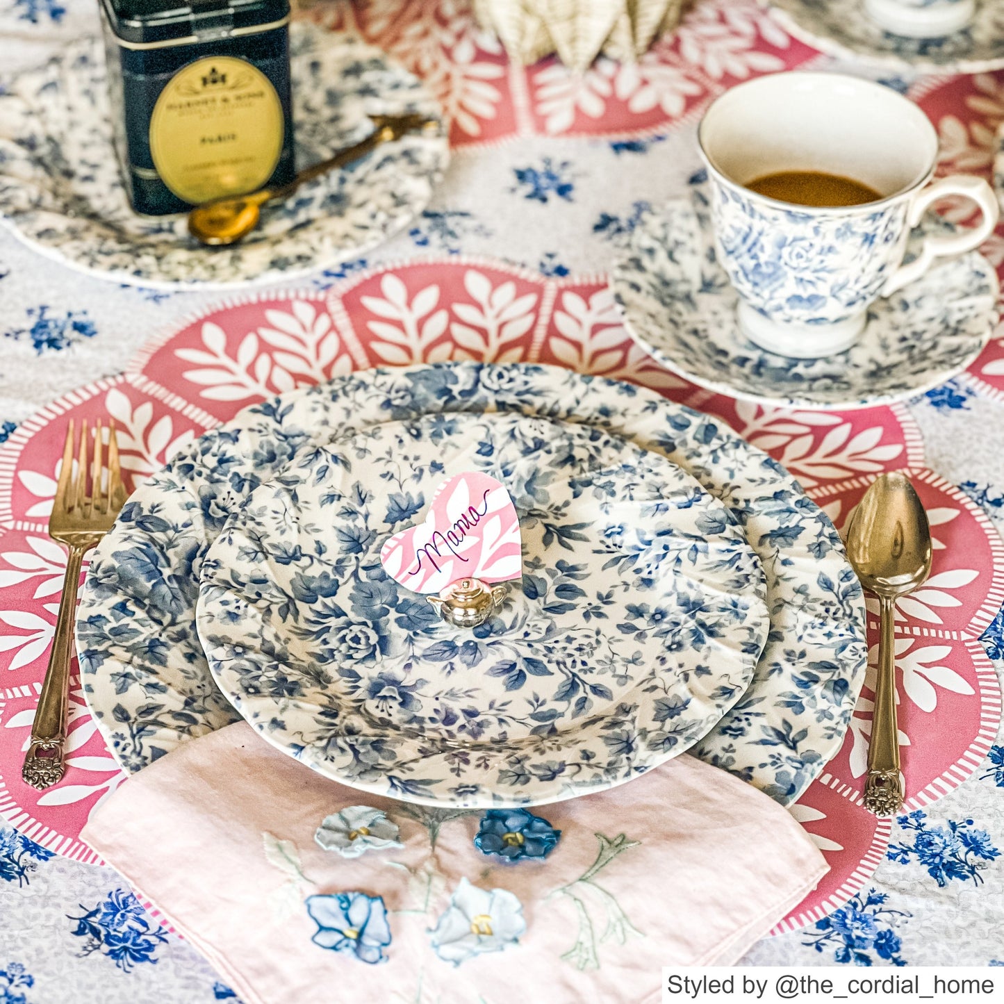 Place setting with a pink and white scalloped round paper placemat layered with blue and white floral dishes and a pink heart place card