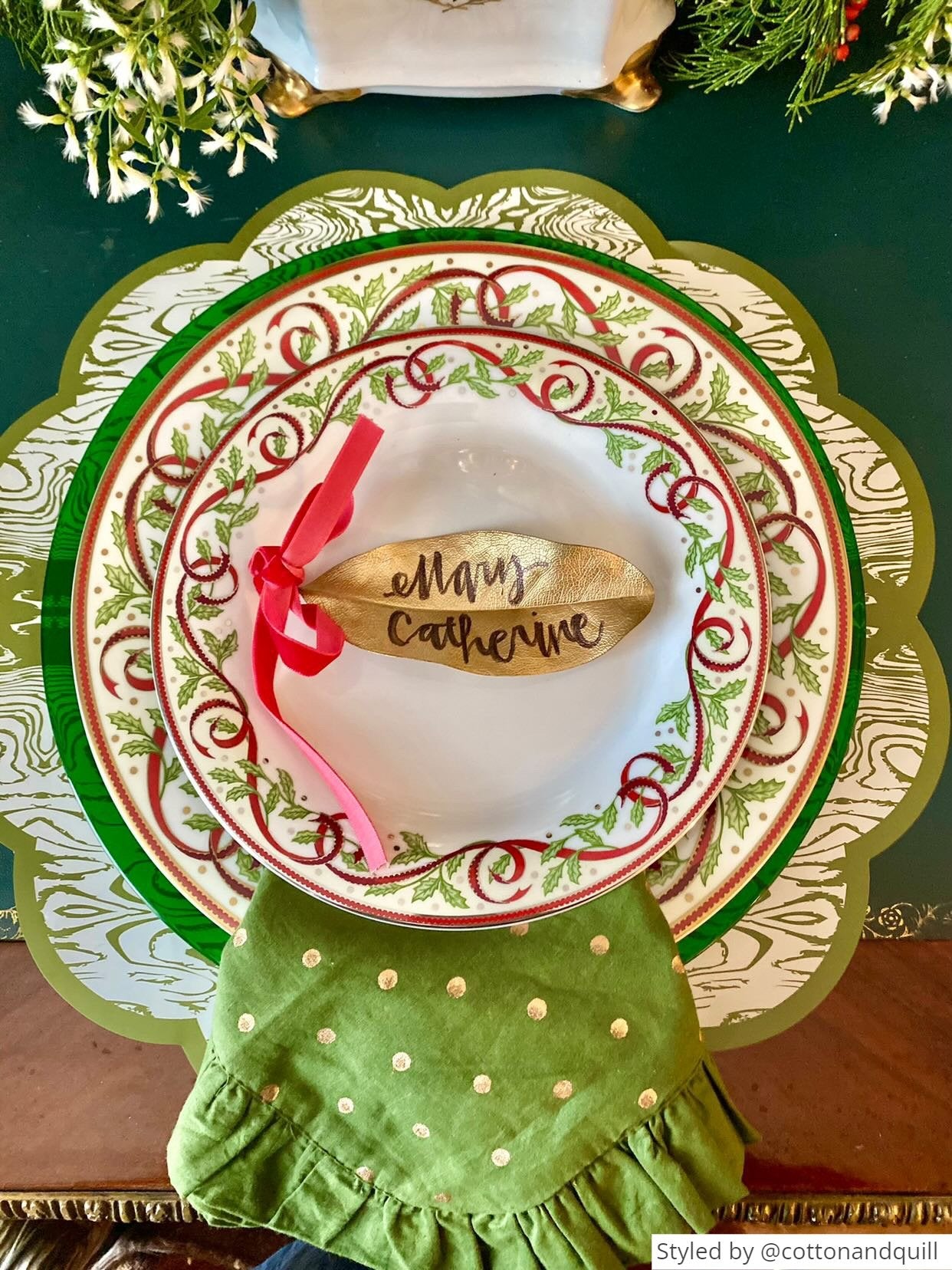 Green wood patterned paper placemat layered with red and green plates and a gold leaf place card