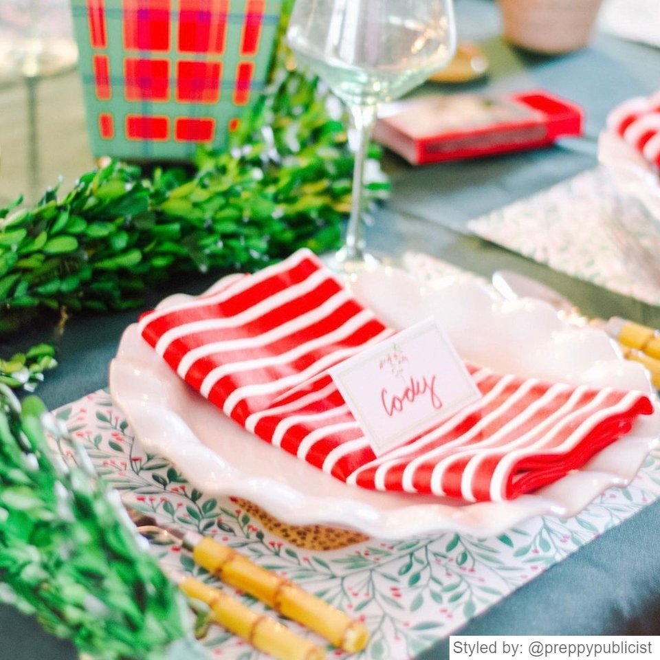 Red and green paper placemat layered with a white plate, red and white striped napkin and a place card