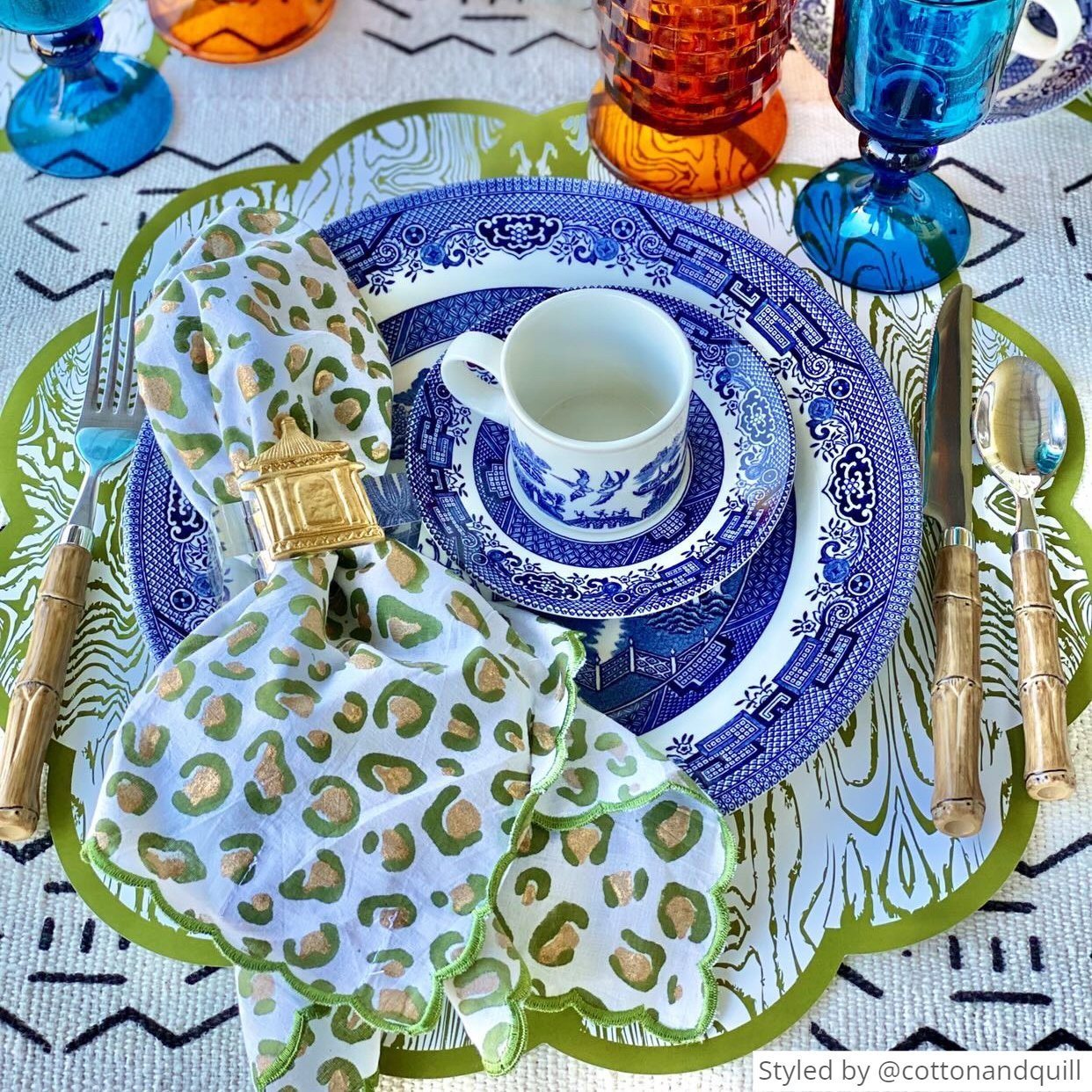 Green wood patterned paper placemat layered a blue and white china set and a green and gold napkin with a gold napkin ring