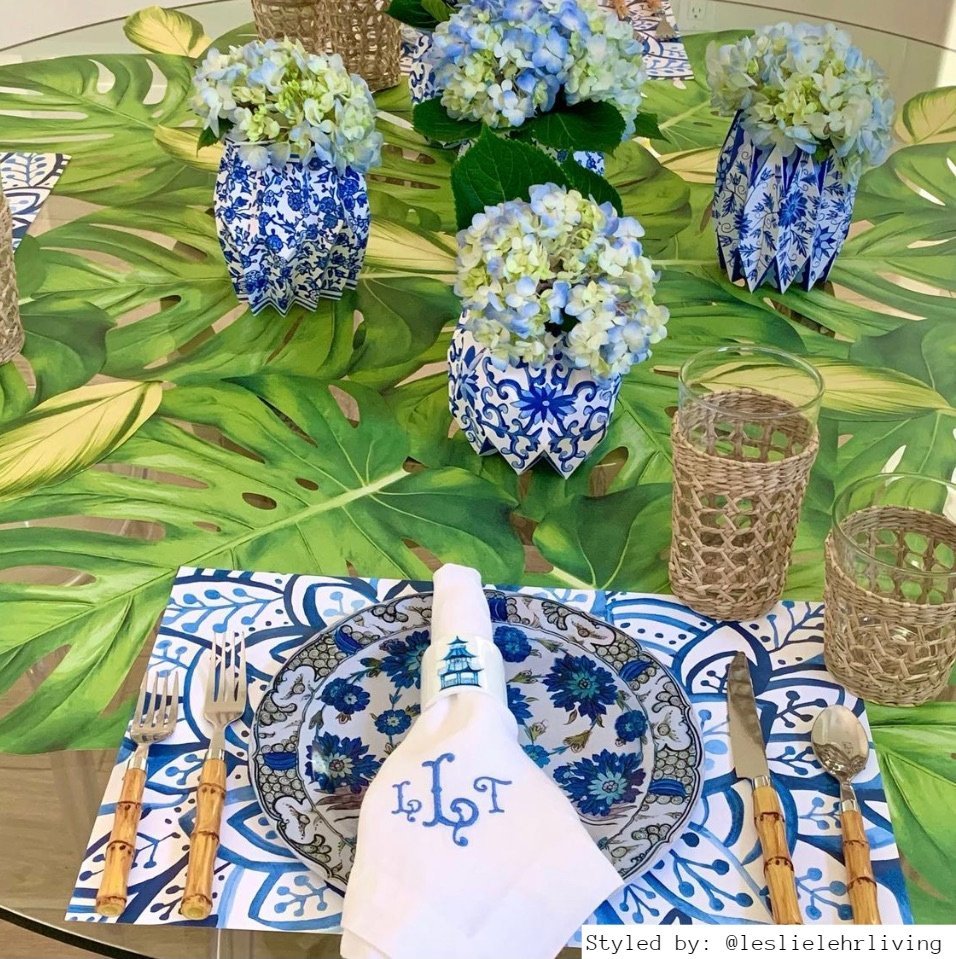 Table setting with blue and white paper placemats on a green leaf tablecloth