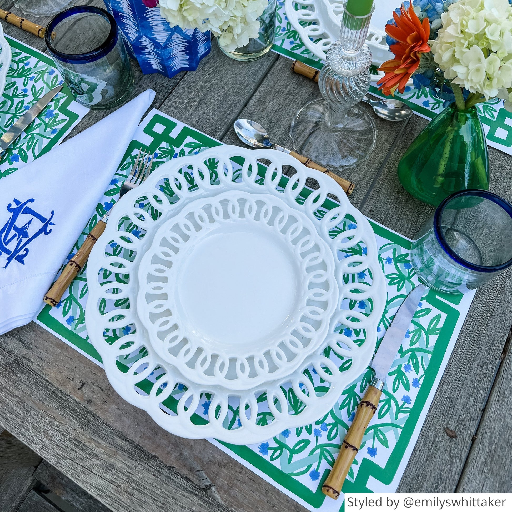 Place setting with green and white paper placemats layered with white plates on an outdoor wooden table