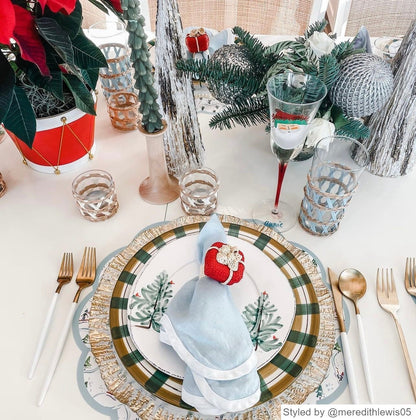 Table setting with a round scalloped paper placemat layered with white and green dishes and a blue napkin with red present napkin ring