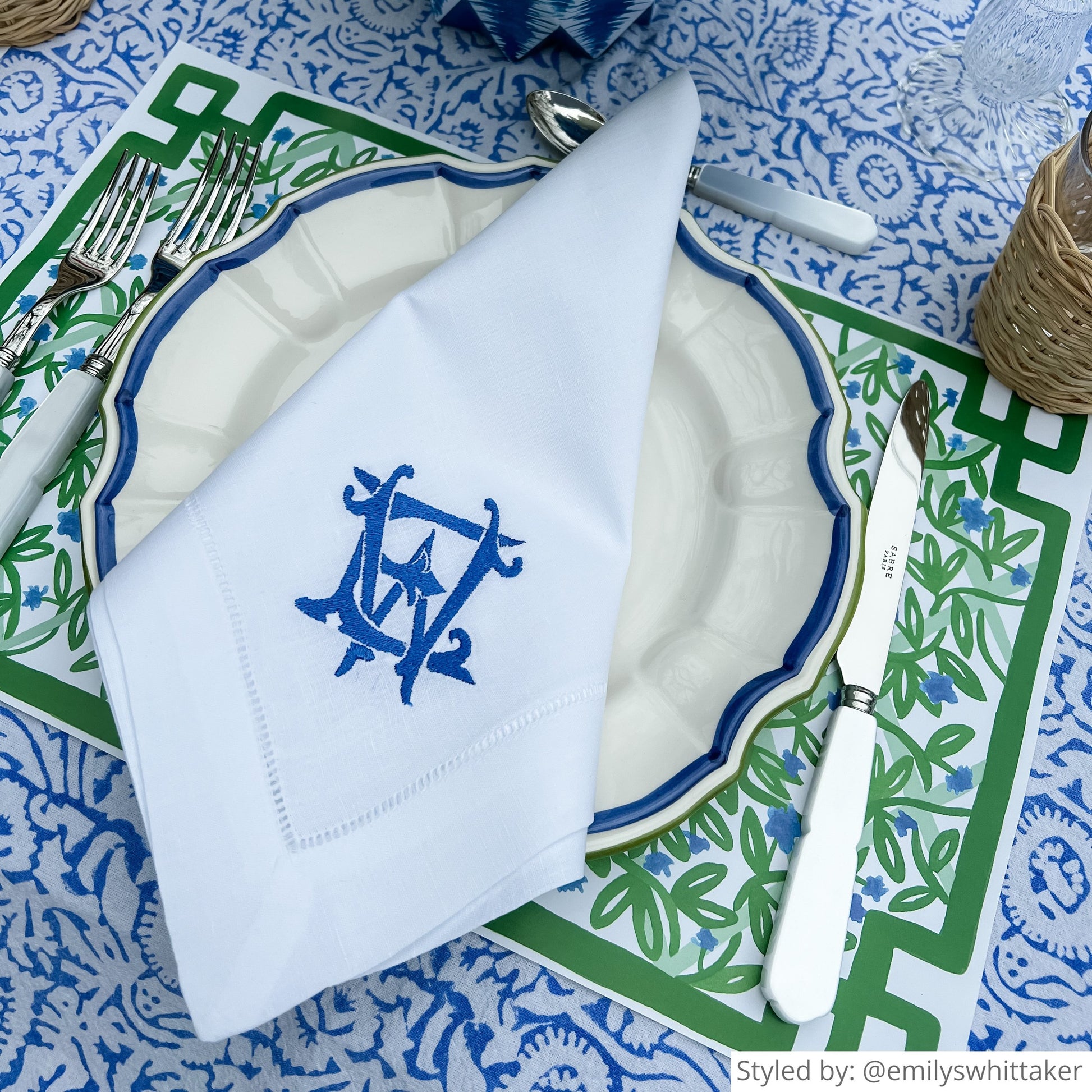 Place setting with a green and white paper placemat layered with a blue and white plate and blue and white napkin on a blue and white floral tablecloth