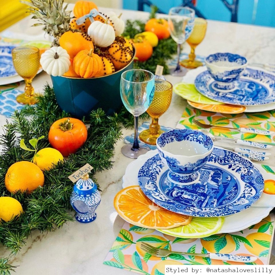 Table setting with orange patterned paper placemats and blue china and teacups and a pumpkin and fern tablerunner