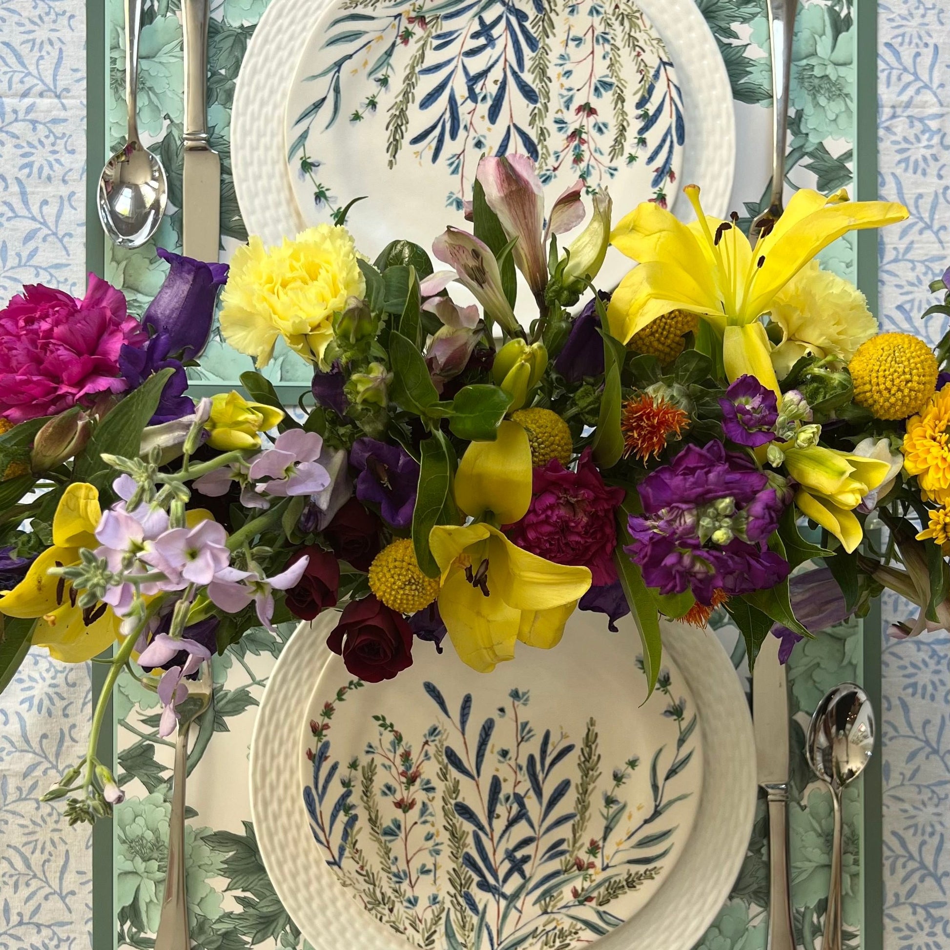 Blue and gray paper placemats layered with white patterned plates fresh flowers