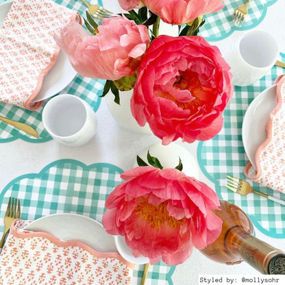 Table setting with green gingham scalloped round paper placemats layered with white plates and pink napkins with pink flower centerpieces