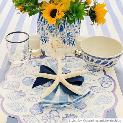 Table setting with a blue and white shell paper placemat layered other blue and white accessories and a white starfish