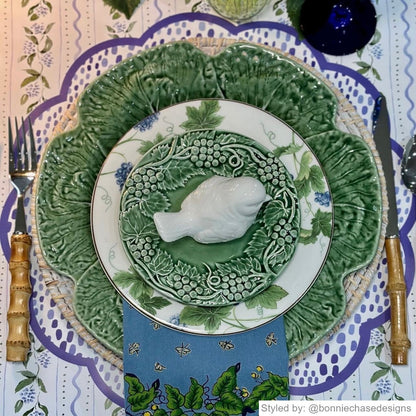 Blue and white dot patterned paper placemat layered with blue and green dishes and a mini bird