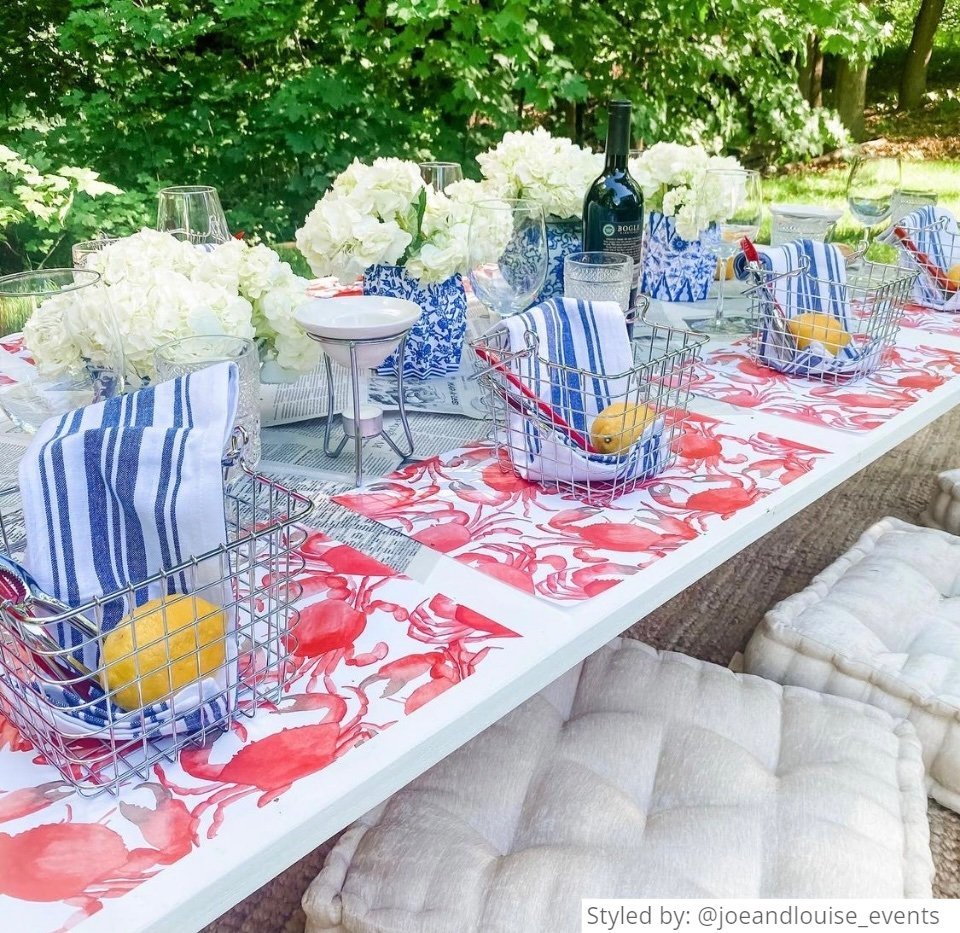 Outdoor table setting with crab paper placemats and white flowers in blue and white paper vases