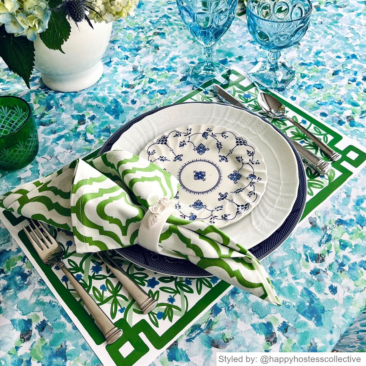 Place setting with a green and white paper placemat layered with blue and white dishes and a green and white napkin on a blue and white tablecloth