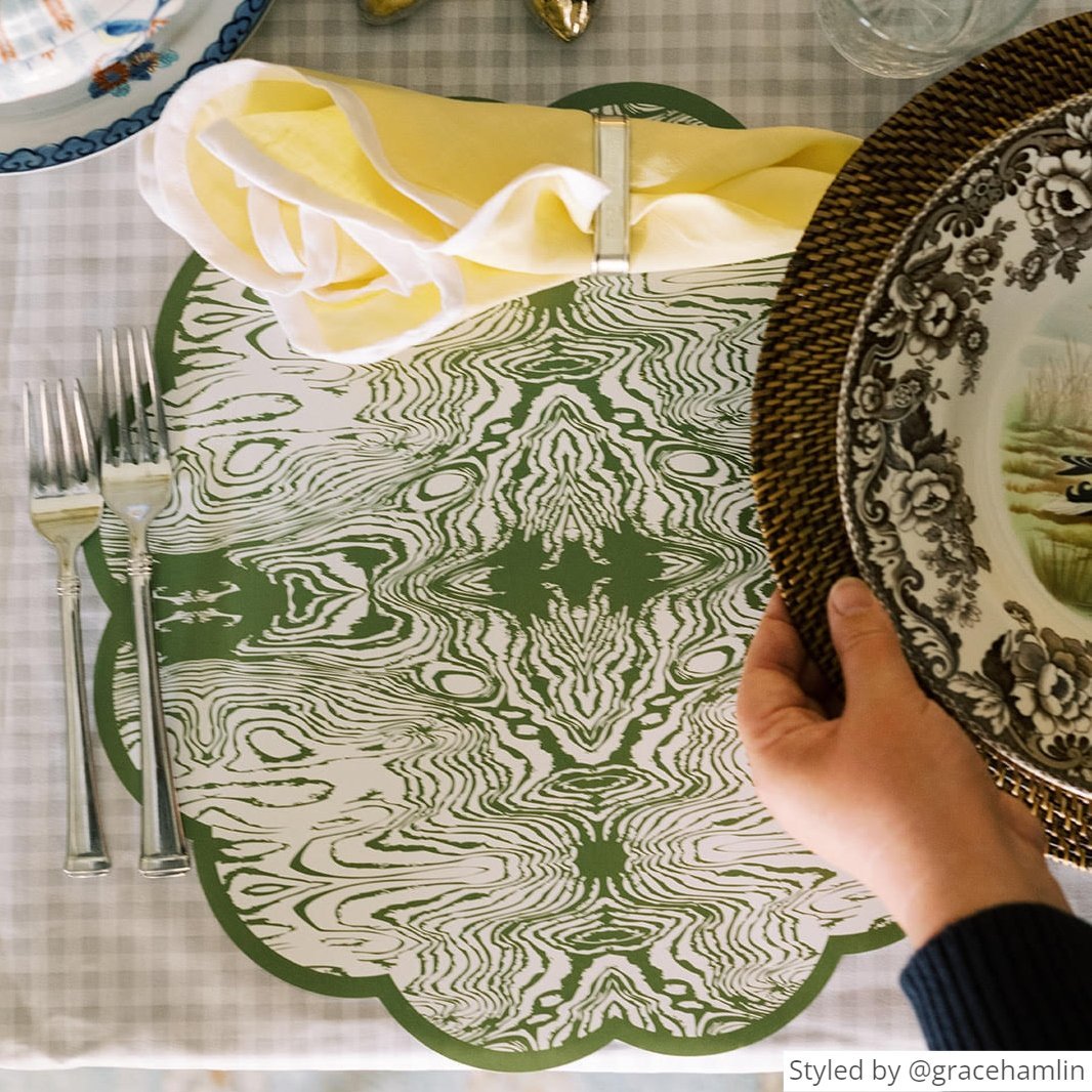 Green wood patterned paper placemat with a yellow napkin on light gray gingham tablecloth with someone putting a plate on top